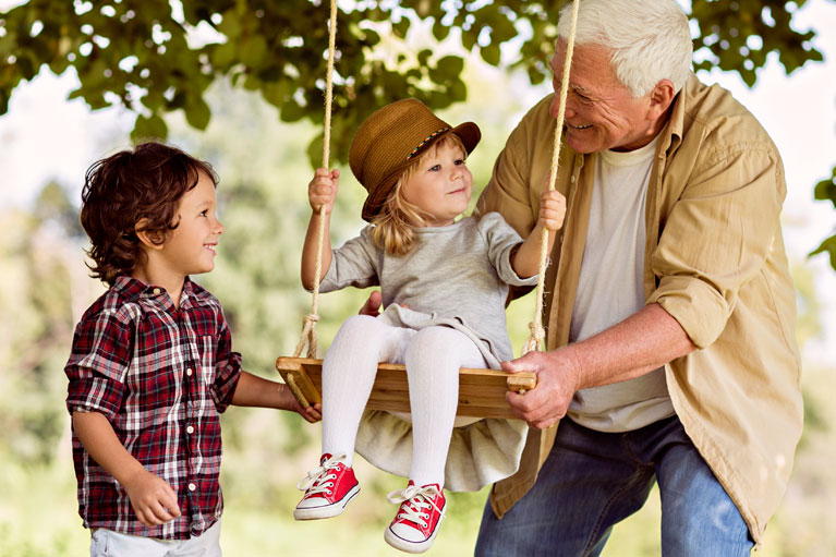 Elderly man pushing a child on a tree swing